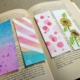 An open book with 4 paper book marks on it. One is purple and blue, one has white stripes, one has red and pink dots, and the other has yellow sunflowers