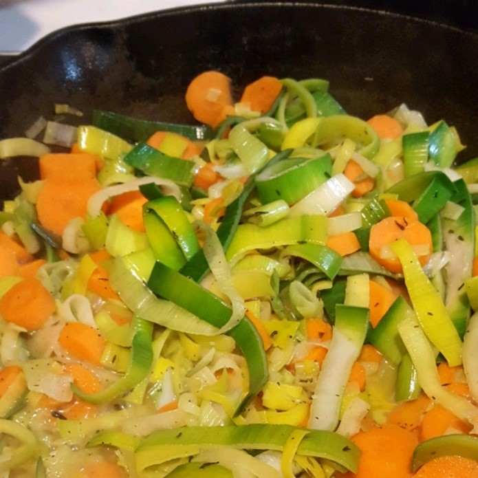 A frying pan with chopped carrots, leeks, and onion in it