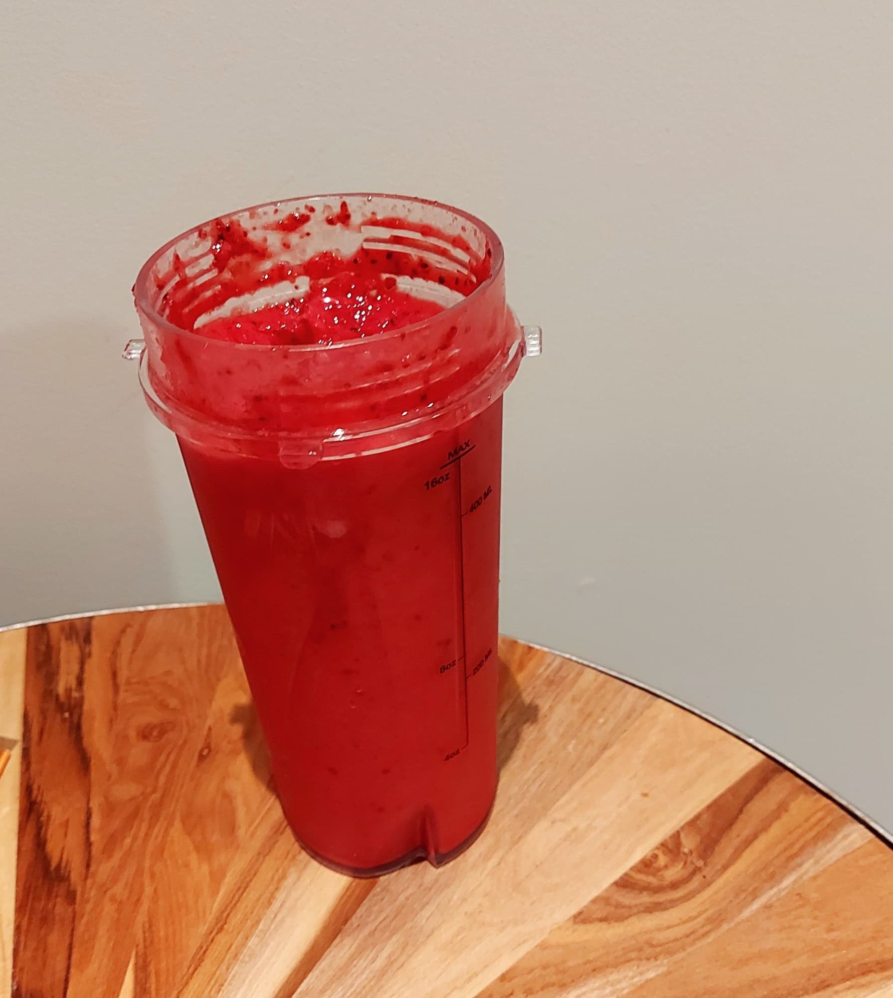 A clear plastic cup with red coloured smoothie inside it